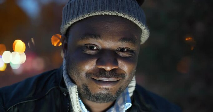 Cheerful african american man in winter hat looks at the camera and smiles shyly, close-up shot