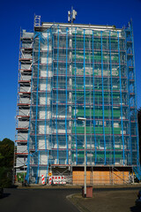 Scaffolded skyscraper with blue and green building tarpaulin in front of bright blue sky, Hannover,...