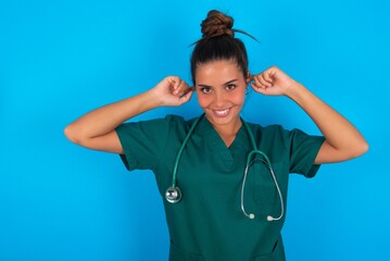 Happy beautiful doctor woman wearing medical uniform over blue background ignores loud music and...