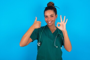 beautiful doctor woman wearing medical uniform over blue background feeling happy, amazed, satisfied and surprised, showing okay and thumbs up gestures, smiling