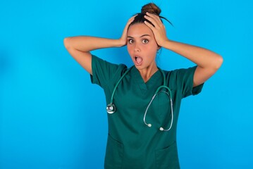 Cheerful overjoyed beautiful doctor woman wearing medical uniform over blue background reacts rising hands over head after receiving great news.