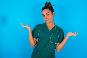 Careless attractive beautiful doctor woman wearing medical uniform over blue background shrugging...
