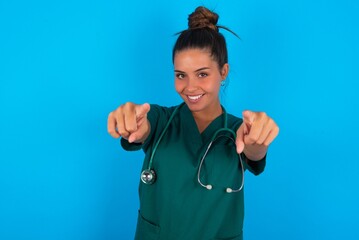 beautiful doctor woman wearing medical uniform over blue background cheerful and smiling poiting at...