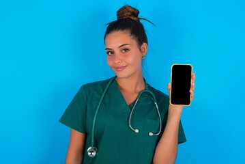 Photo of interested beautiful doctor woman wearing medical uniform over blue background hold telephone look side empty space screen