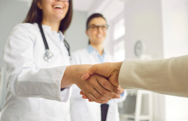 Close up of hands of positive woman doctor and hospital patient making handshake as token of gratitude to therapist in white coat working in clinic for quality treatment. Selective focus