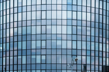 High office modern building with many small glass windows with blue sky reflection in facade