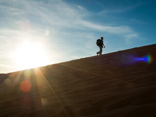 Adventurer climbs a sand dune against the backdrop of the setting sun