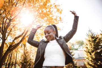 African american woman with dark hair dancing having fun outside autumn city park blur yellow leaves background. Fall time
 - obrazy, fototapety, plakaty