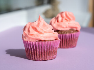 Cupcake with a lush pink cream cap on a purple table, with a place for text