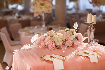 table decoration with pink tablecloth, crystal candlesticks with candles and white pink flowers in restaurant . stylish wedding day. setting table with gold plate, fork and knife