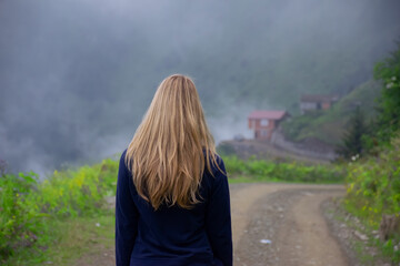 Girl walking alone on mountain highway in Spring foggy day.