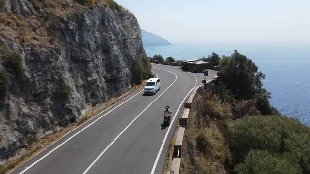 Young guys ride a motorcycle along the road along the Amalfi coast Italy on the Mediterranean Sea. Drone follows moto. Travel destination in Italy. August 2022
