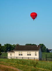 Hot air balloons rise in the sky behind an Amish school in the early morning hours of on a summer day. 