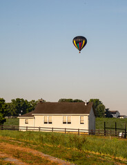 Fototapeta na wymiar Hot air balloons rise in the sky behind an Amish school in the early morning hours of on a summer day. 