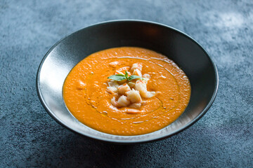 Pumpkin cream soup with shrimp on black bowl selective focus