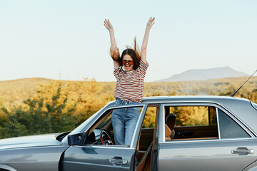 Happy woman traveler climbed on the car and spread her arms smiling happily. looks at the nature around. Lifestyle in travel and joy