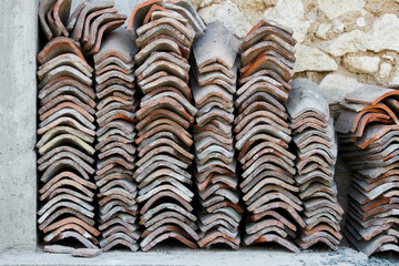 old ceramic tiles for the roof of the house are stacked in rows near the wall for use in repairs. red clay, utilitarian ceramics in everyday life and construction.