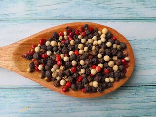 Peppercorns: black, white and pink, in a wooden spoon, isolated on a wooden table, selective focus with space for text.