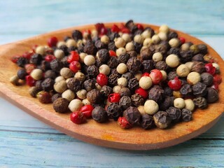 Peppercorns: black, white and pink, in a wooden spoon, isolated on a wooden table, selective focus with space for text.