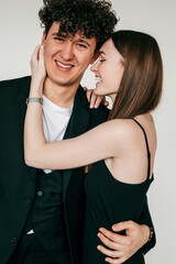 Closeup portrait of happy loving couple in black outfits for event, gray studio background. Smiling guy and elegant girl gently snuggling and passionately embracing. Intimate relations and feelings