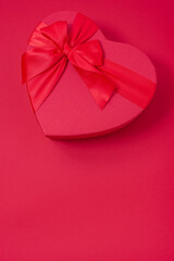 Overhead on a red vertical background lies a large red box in the shape of a heart with a bow, a greeting card for Valentine's Day, valentine, screensaver for the phone screen