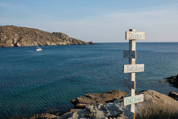 View of wooden signs for Take away, Live music, acai, cold brew, vegan, smoothies  and the sea in the background on the beach of Mylopotas in Ios Greece