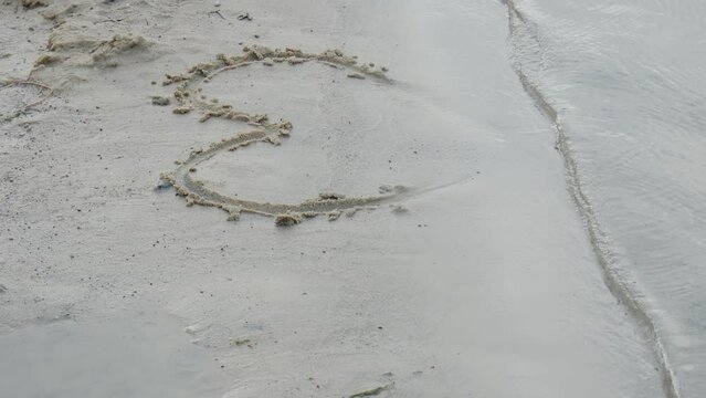 Sea. A heart is drawn on the sand. Water washes away the writing on the sand