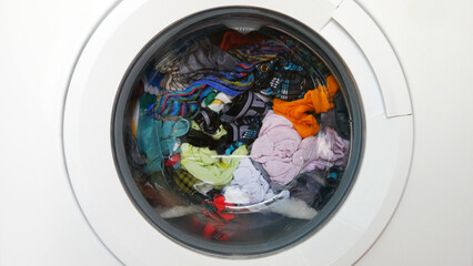 Close-up of the drum of a washing machine with various colored clothes inside of it