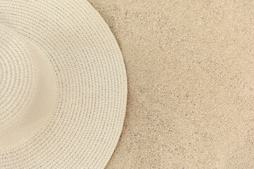 Fototapeta na wymiar Yellow straw women's hat lies on the sand, top view, half of the hat