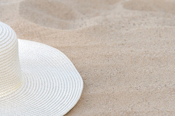 A female straw white hat lies on a yellow sandy seashore under sunlight