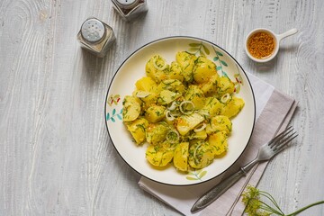 A simple boiled potato salad with onions, dill and mustard dressing in a white bowl on a light wooden background. Scandinavian style, food.