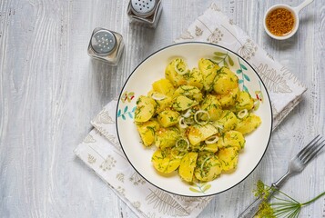 A simple boiled potato salad with onions, dill and mustard dressing in a white bowl on a light wooden background. Scandinavian style, food.