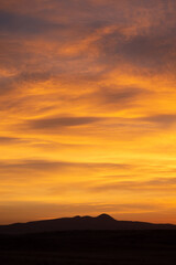 Obraz premium Vivid yellow sunrise over silhouette mountain peak range vertical
