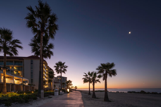 A beach path on Coronado beach, San Diego, at sunrise.  The sky is turning orange and the moon can still be seen in the sky. 
