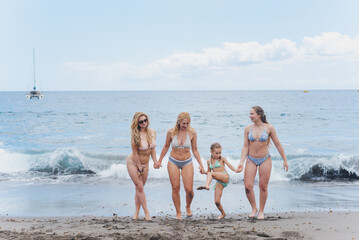 Mom and her daughters have fun, posing on the ocean. Family on vacation by the sea. Travel concept, all together. Atlantic ocean and sky horizon. Sea waves.