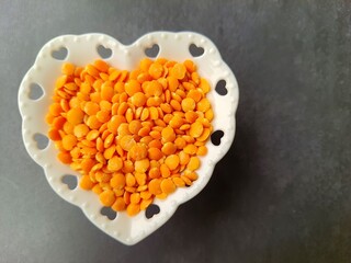Lentils (Lens culinaris): Red in heart-shaped crockery bowl, isolated on black background, top view, space for text.