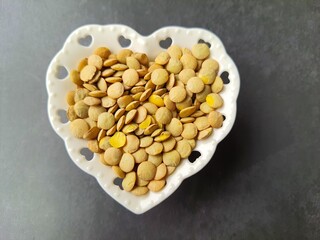 Lentils (Lens culinaris): Brown in heart-shaped crockery bowl, isolated on black background, top view, space for text.