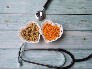 Lentils: brown and red in heart-shaped white crockery bowls and stethoscope, isolated, on wooden...