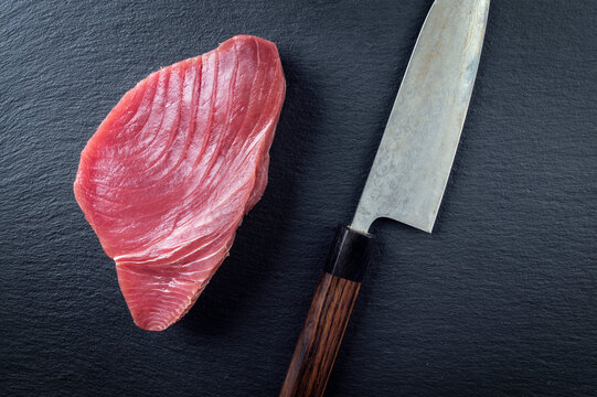 Traditional Japanese raw tuna steak with a Japanese deba knife served as top view on a design stone board with copy space