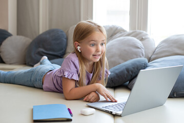 A cute girl is enjoying a movie on her laptop. Little girl watch online videos with headphones in the nursery. Online lesson for a student,lesson with a tutor