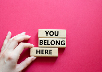 You belong here symbol. Wooden blocks with words You belong here. Beautiful red background. Businessman hand. Business and You belong here concept. Copy space.