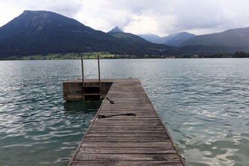 Wooden pier, wharf without boats on Lake Wolfgangsee. The peaks of the Alps are visible in the background.