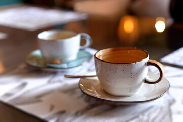 Orange and blue cups on saucers. The mugs with tea in soft focus standing on menu papers on...