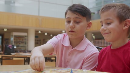 4K. Children play a board game in the library, sitting at the table.