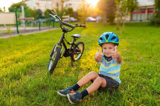 Happy boy in bike a hemlet in the park near his bicycle. Active child. Summer time. Protection.