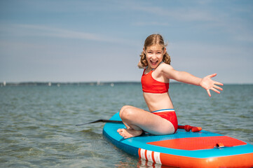 Happy teen child girl having fun on sup board in sea at summer holidays