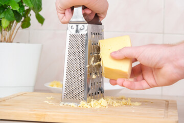 A man rubs cheese on a metal grater for freezing and further cooking pizza, pasta.