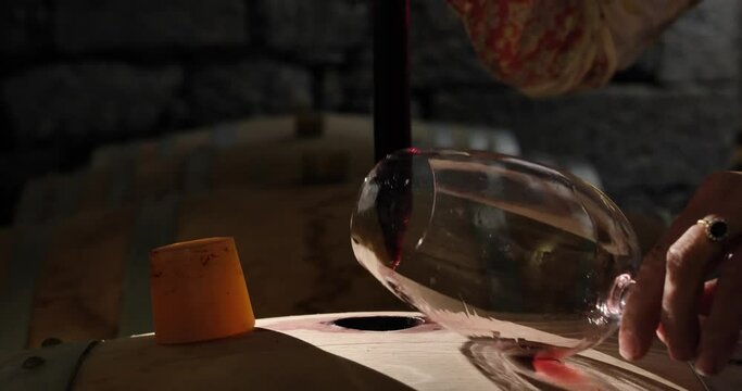 Female winemaker checking on wine by sampling pipette . Woman testing wine in a factory or warehouse
