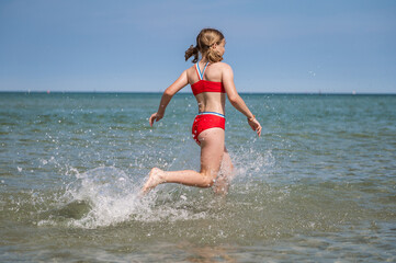 Happy teen girl running and splashing water in turquoise sea at summer holidays