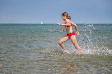 Beautiful child girl playful running in water at sea